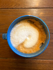 A blue cup of cappuccino stands on a wooden table