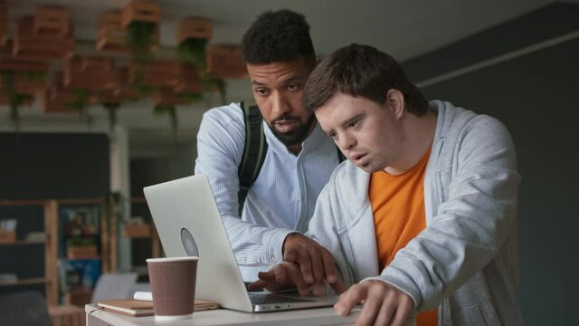 Happy young man with Down syndrome and his tutor using lapotp indoors at school.