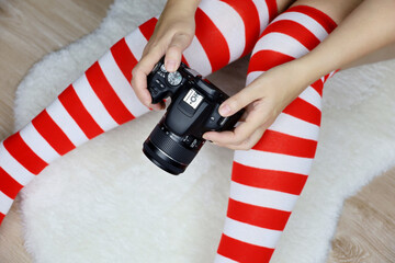 Woman in Christmas knee socks sitting on white fur rug with DLSR camera in hands. Concept of...