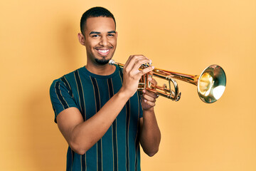 Young african american man playing trumpet smiling with a happy and cool smile on face. showing...