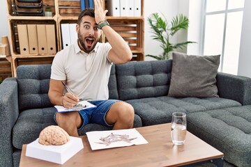 Fototapeta premium Handsome hispanic man working with rorschach test at psychology clinic surprised with hand on head for mistake, remember error. forgot, bad memory concept.