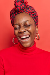 Vertical image of overjoyed dark skinned young woman laughs gladfully has carefree expression wears...