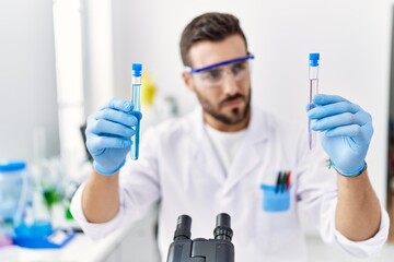 Young hispanic man wearing scientist uniform holding test tube at laboratory