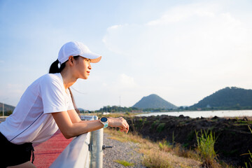 Fototapeta na wymiar Female athlete tying laces for jogging on road in minimalistic barefoot running shoes at public park near mountain. Active Asian woman relax after running.