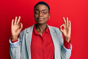 Naklejka premium Young african american woman wearing business jacket and glasses relax and smiling with eyes closed doing meditation gesture with fingers. yoga concept.