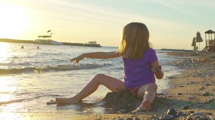 little girl on seashore, collects stones and throws them into water.