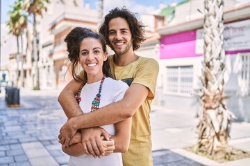 Naklejka premium Man and woman couple smiling confident hugging each other at street