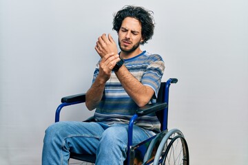Handsome hispanic man sitting on wheelchair suffering pain on hands and fingers, arthritis...