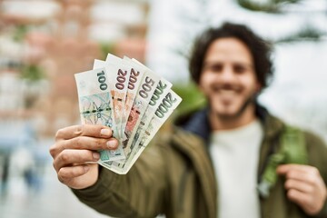 Handsome hispanic man holding czech crown banknotes at the city