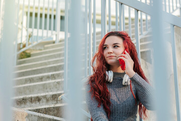 19 year old young woman with wavy red hair using her mobile phone to make a call outdoors. lifestyle, city life and technology concept.