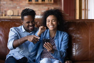 Happy young African ethnicity multiracial couple looking at phone screen, reading email with amazing news, celebrating online lottery win or getting auction giveaway results, internet success concept.