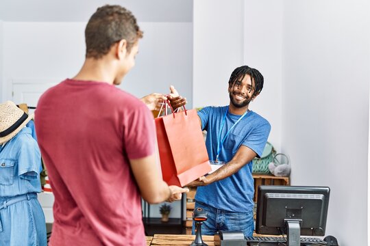 Two men shopkeeper and customer holding shopping bags at clothing store