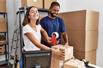 Man and woman business partners packing package using tape at storehouse