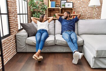 Man and woman couple relaxed with hands on head sitting on sofa at home