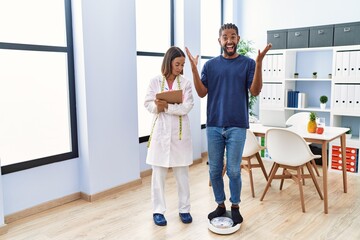 Obraz premium Dietitian at the clinic with client checking weight celebrating victory with happy smile and winner expression with raised hands