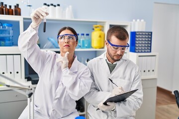 Man and woman scientist partners write on clipboard holding test tube working at laboratory