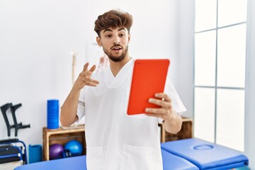 Young arab man wearing physiotherapist uniform having video call at clinic