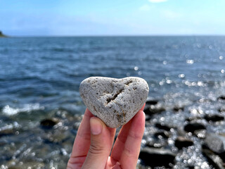 Heart shape stone in girls hand against background of beach. Summer sunny day. Love, wedding and Valentine day concept. Finding beautiful and interesting stones. Beach vacation. 