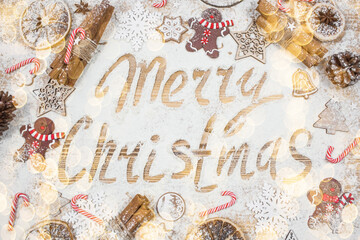 The inscription on the flour Merry Christmas. A frame of gingerbread men, cinnamon, cookies, lollipops and Christmas decorations on a wooden background. The concept of cafes and restaurants. 