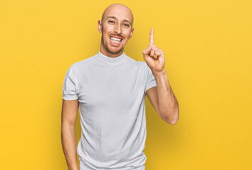 Bald man with beard wearing casual white t shirt showing and pointing up with finger number one while smiling confident and happy.