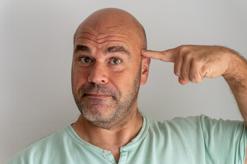 Close-up of face of caucasian man, with beard and bald man gesturing with the index finger of the hand touching the top of the head.Isolated on white background.