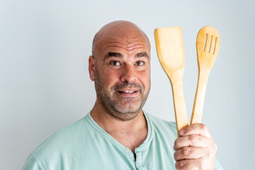 Face of a bald and bearded Caucasian man, with some wooden spoons in his hand. 