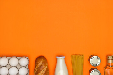 Glass bottle of milk, white eggs, spaghetti, olive oil, bread, metal tin on bright orange background