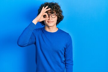 Fototapeta na wymiar Handsome young man wearing casual clothes and glasses doing ok gesture with hand smiling, eye looking through fingers with happy face.