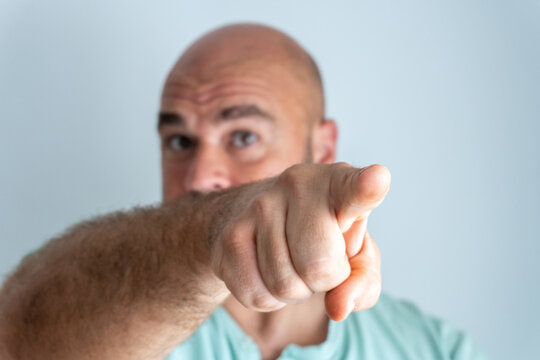 Close-up of a bald, bearded, caucasian man face, gesturing and accusing with the index finger.