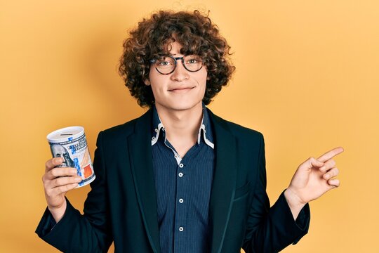 Handsome young man holding piggy bank smiling happy pointing with hand and finger to the side