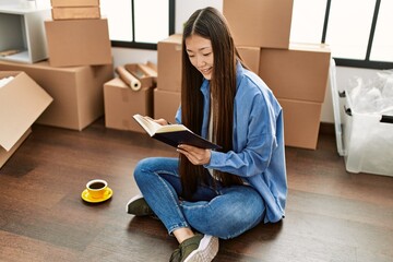 Obraz premium Young chinese girl reading book and drinking coffee at new home
