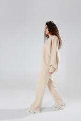 Young woman with afro hairstyle in modish sweatshirt and pants walking across a white background