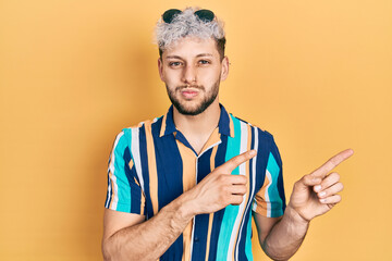Young hispanic man with modern dyed hair pointing with fingers to the side puffing cheeks with...