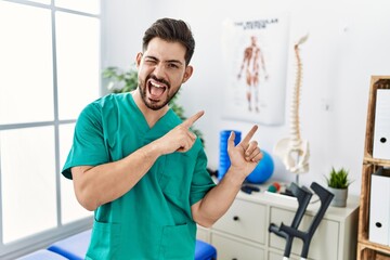 Naklejka na ściany i meble Young man with beard working at pain recovery clinic smiling and looking at the camera pointing with two hands and fingers to the side.