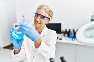 Middle age blonde woman wearing scientist uniform holding test tube at laboratory