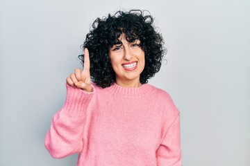 Young middle east woman wearing casual clothes showing and pointing up with finger number one while smiling confident and happy.