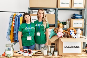 Two young women wearing volunteer t shirt at donations stand thinking attitude and sober expression...