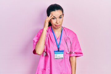 Young brunette woman wearing doctor uniform and stethoscope worried and stressed about a problem with hand on forehead, nervous and anxious for crisis