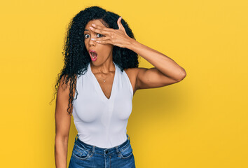 Middle age african american woman wearing casual style with sleeveless shirt peeking in shock covering face and eyes with hand, looking through fingers with embarrassed expression.