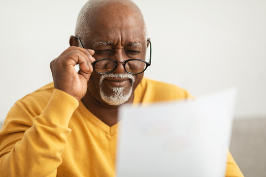Senior African Man Squinting Eyes Reading Papers Wearing Eyeglasses Indoor