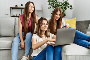 Three young hispanic woman smiling happy using laptop and credit card sitting on the sofa at home.