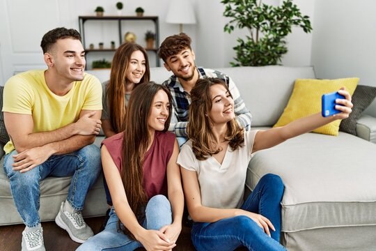 Group of young friends smiling happy make selfie by the smartphone sitting on the sofa at home.