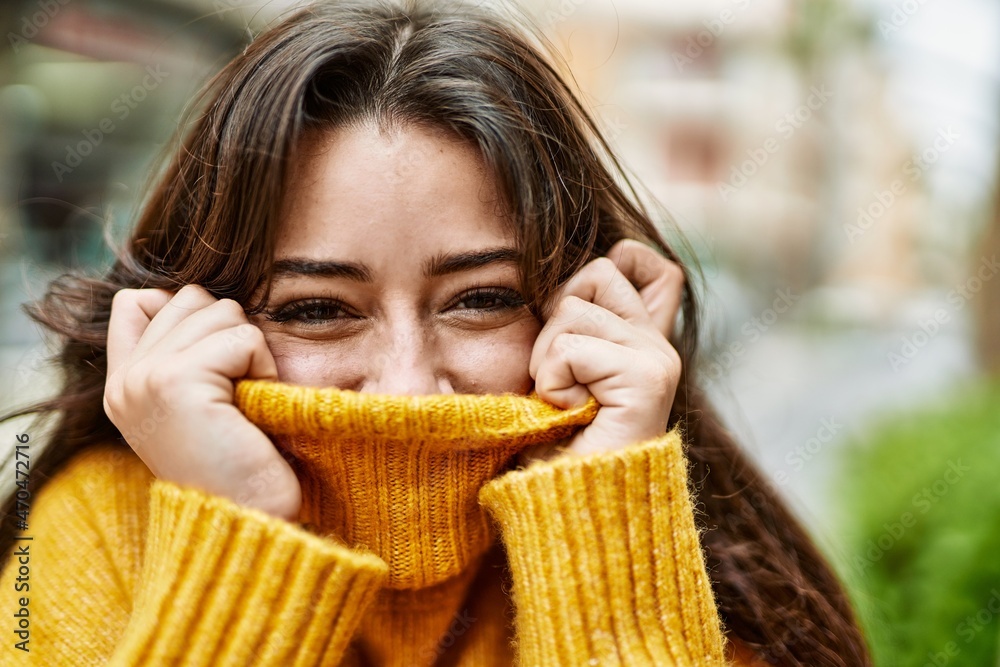 Wall mural Young beautiful brunette woman wearing turtleneck sweater doing funny gesture covering face with sweater