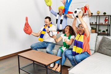 Group of middle age friends watching and supporting soccer match at home.