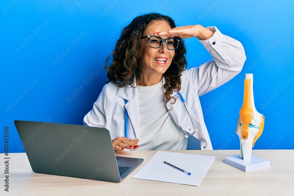 Poster Beautiful middle age woman doctor at orthopedic clinic very happy and smiling looking far away with hand over head. searching concept.