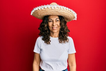 Middle age hispanic woman holding mexican hat looking positive and happy standing and smiling with a confident smile showing teeth