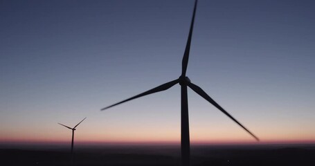 AERIAL VIEW: two rotating silhouettes of wind turbine propellers against the night sky. Eco-friendly generation of electricity from wind energy. Concept of renewable energy sources.