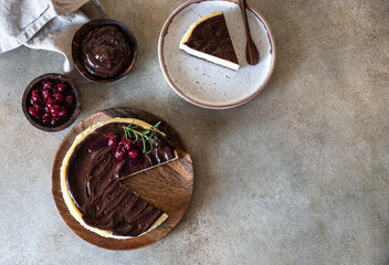 Classic creamy cheesecake with chocolate ganache, cherries and rosemary on concrete background....