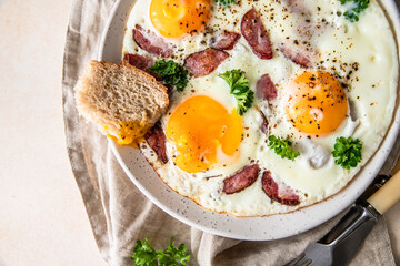 Fried eggs with sausage and parsley on a ceramic plate served with bread, light background. Classic breakfast.