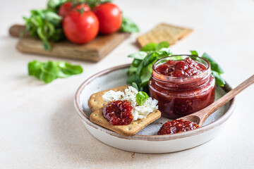Tomato jam, confiture or sauce in glass jar with crackers and green leaves salad. Unusual savory jam. Mediterranean cuisine.